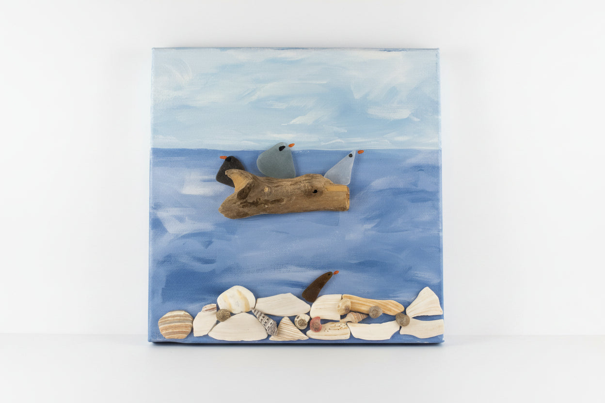Handmade sea glass seagulls perched on driftwood above shells on a blue ocean canvas, coastal wall art
